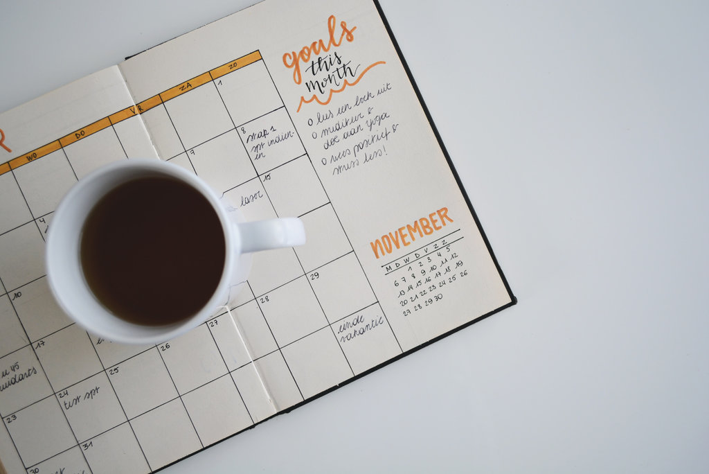 White ceramic coffee mug on top of a planner titled “goals this month”.