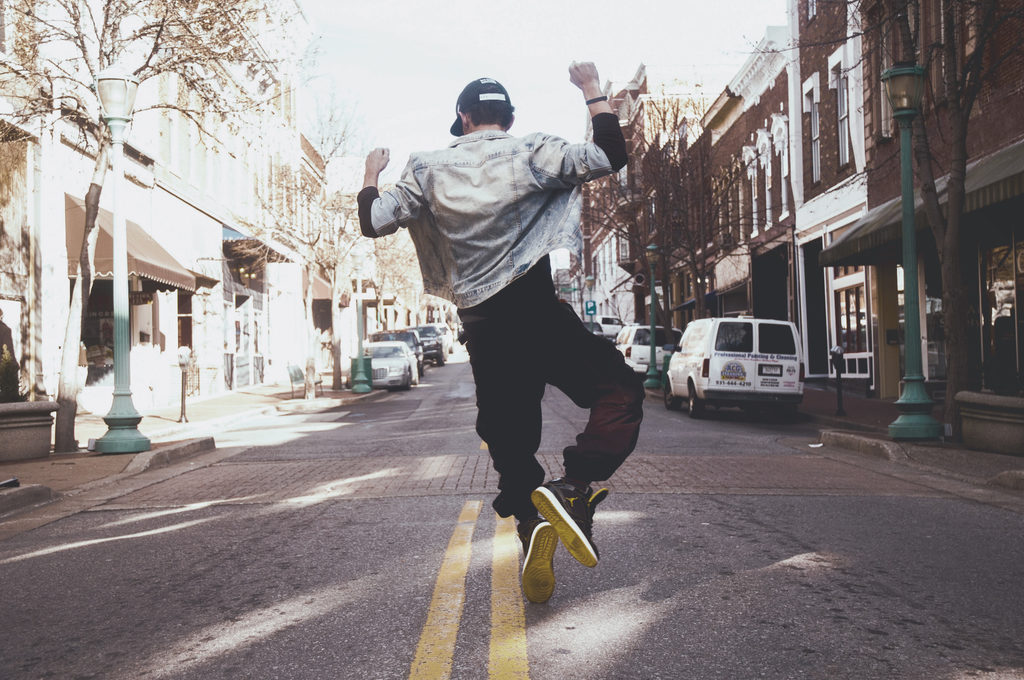 Man jumping in celebration on the middle of the street during daytime.