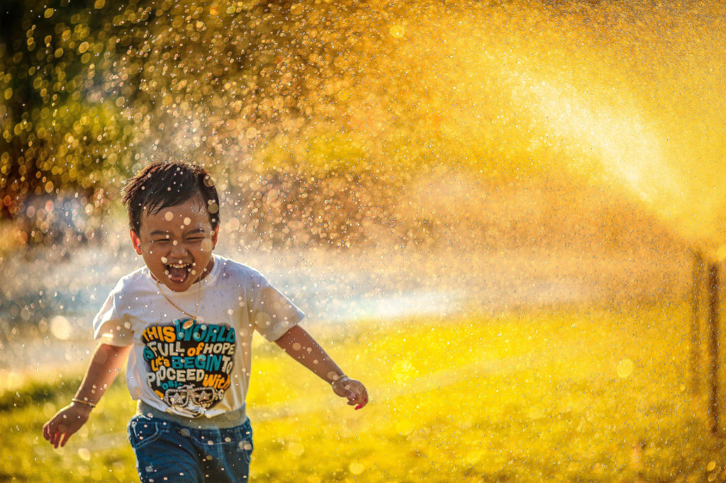 A boy joyfully running through sprinklers.