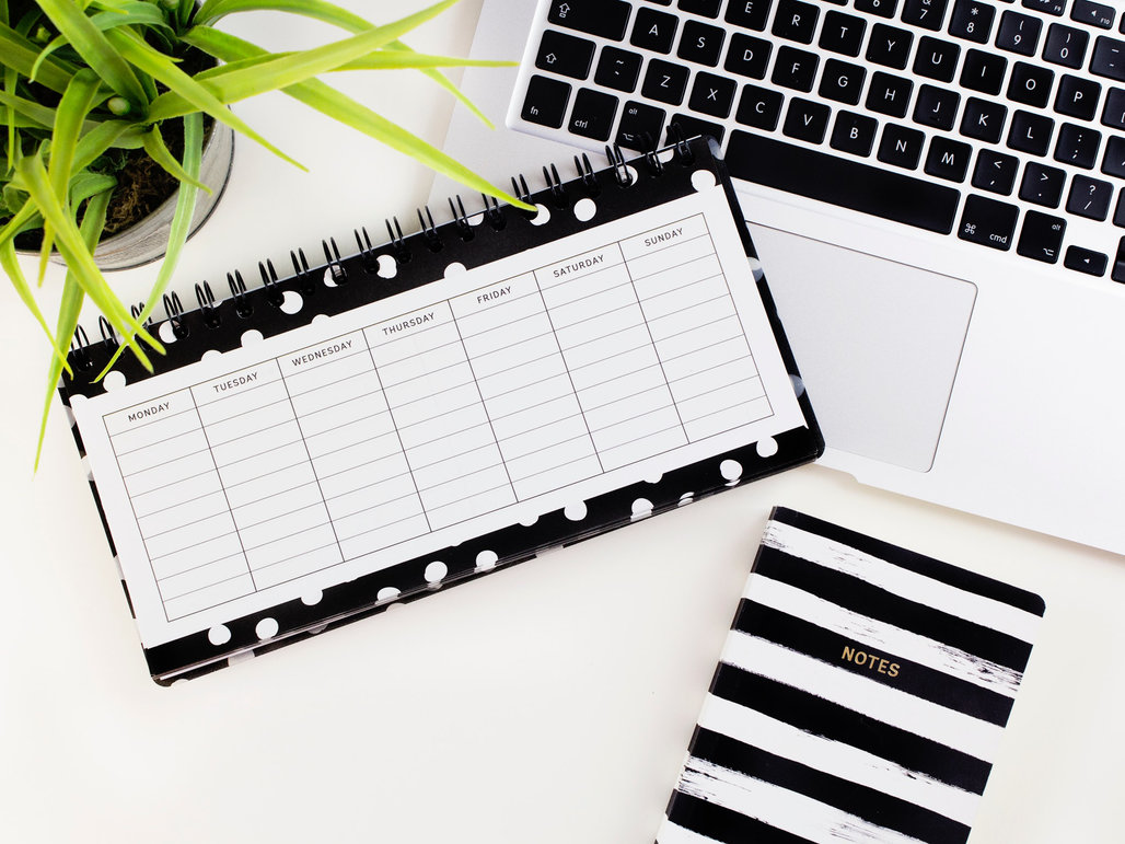 An empty weekly planner on a white desk partly covering a laptop keyboard.