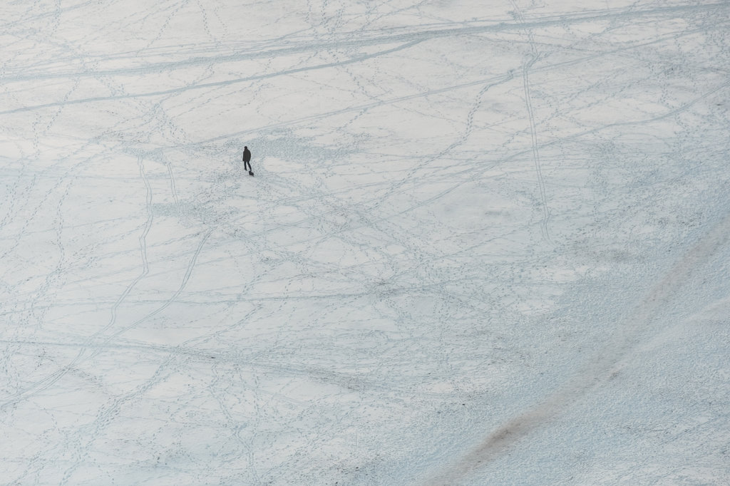 Aerial view of a person walking on a snow-covered ground with footprints leading in different directions.
