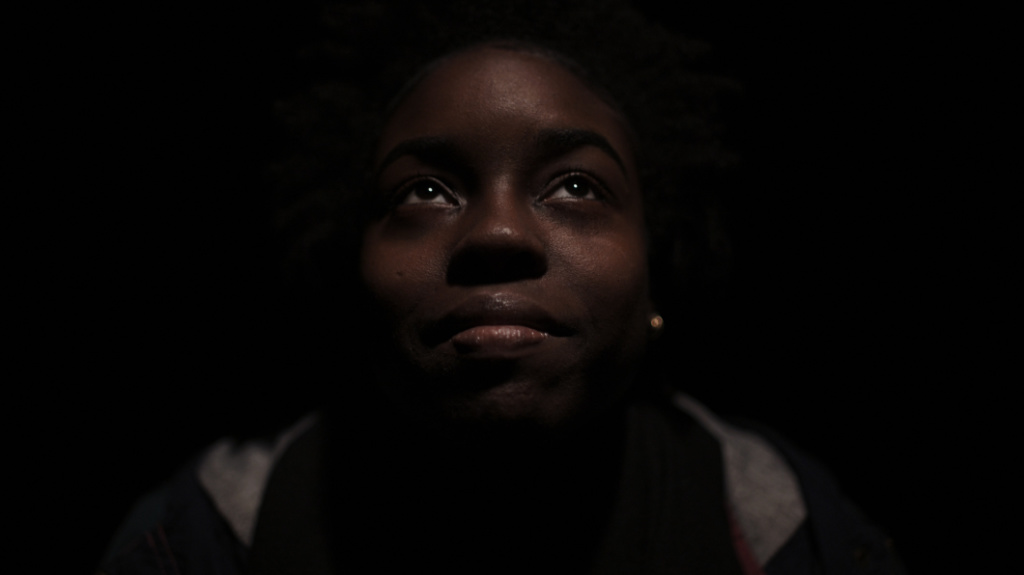 A woman surrounded by darkness looking up.