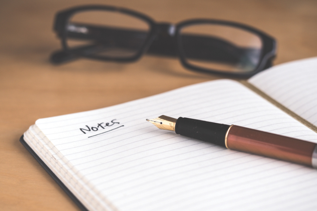 A brown fountain pen on a notebook with a handwritten, underlined title "Notes".