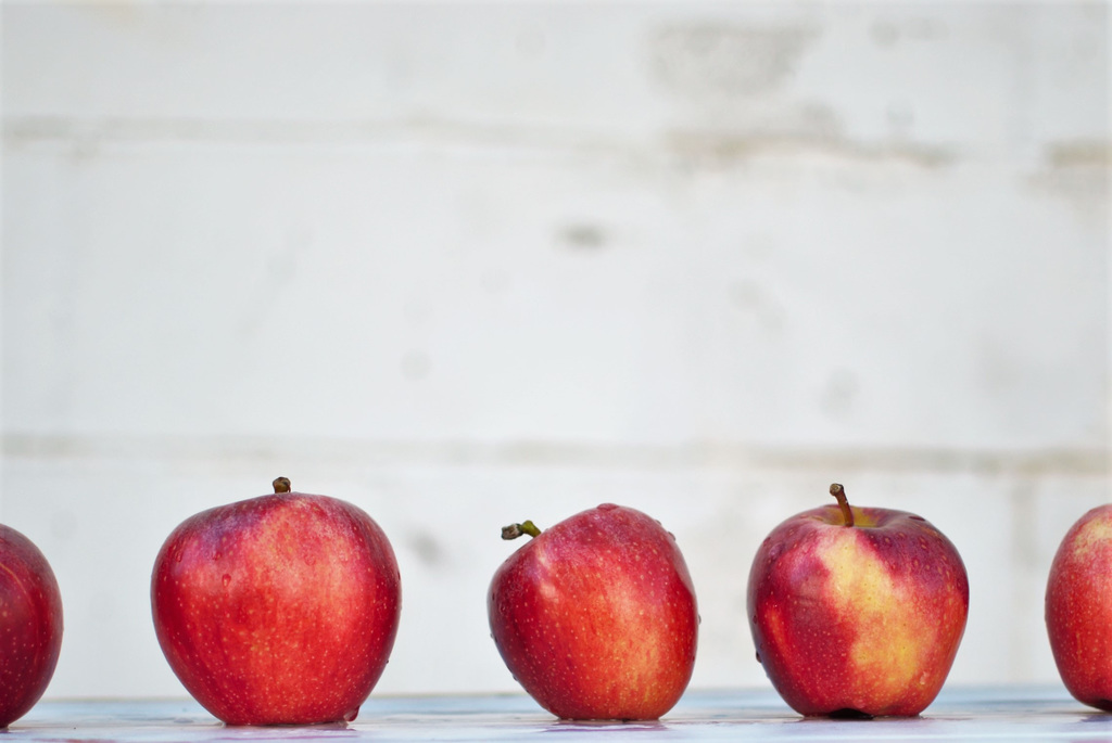 Five oddly shaped red apples on a white surface.