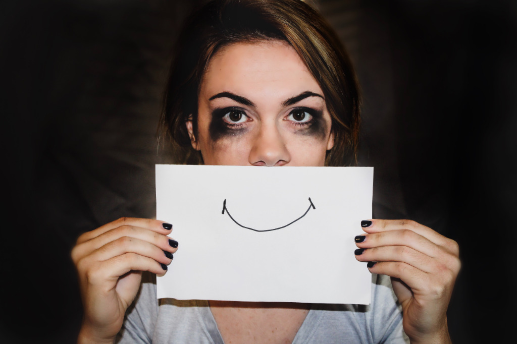 A depressed person holding a white paper over their head with a hand-drawn smile.