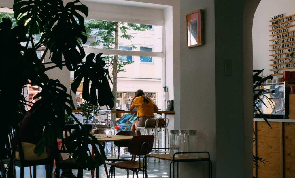 A woman holding her head sitting on a chair behind a laptop.