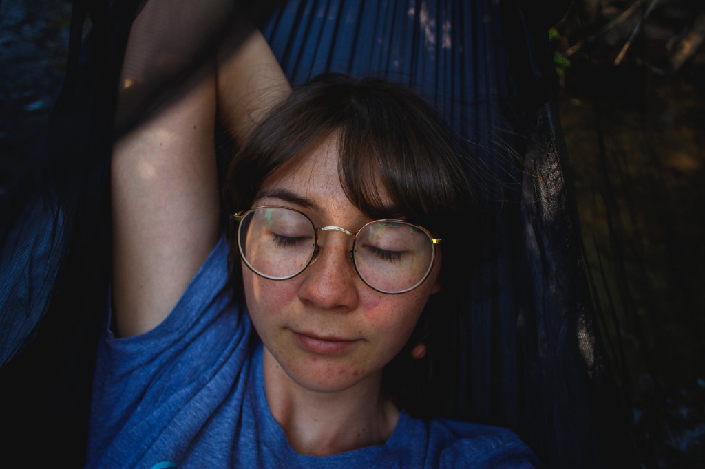 A woman in a blue t-shirt resting in a hammock.