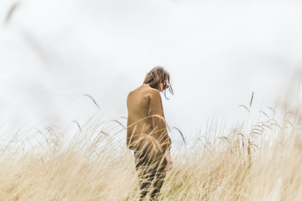 A person standing in the middle of a wheat field, looking into the ground.