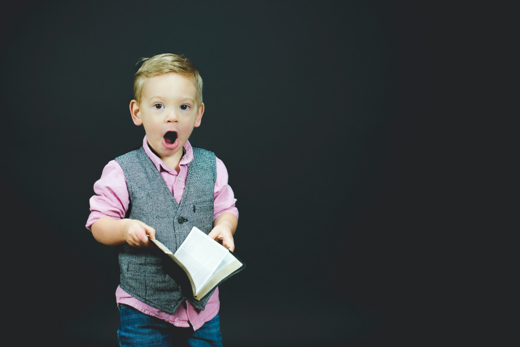 A boy holding a book with a surprised look on his face.